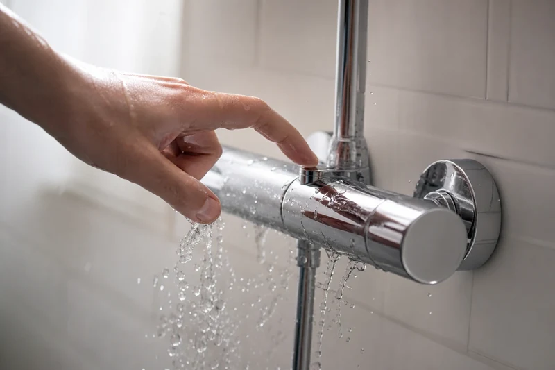 Main qui règle la température de l'eau autour de 30 °C sur un mitigeur de douche