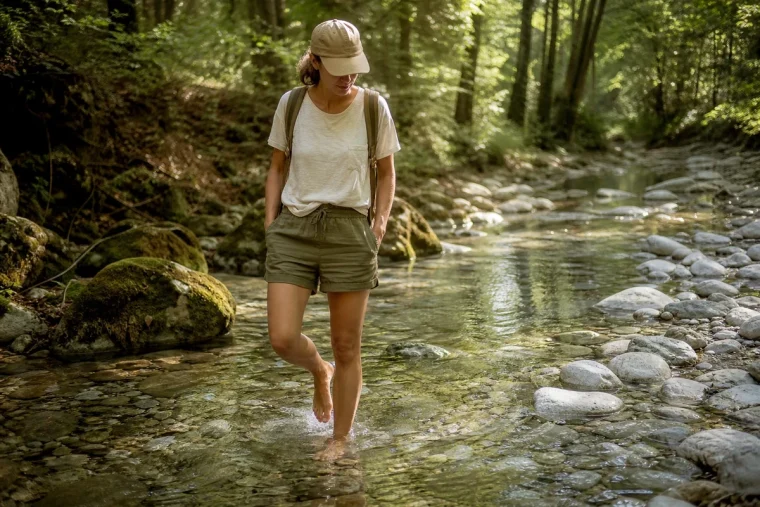 Femme marchant pieds nus dans une rivière fraîche au cœur d'une forêt française en été