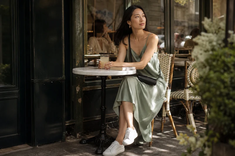 Femme en robe nuisette vert sauge et baskets blanches en terrasse parisienne