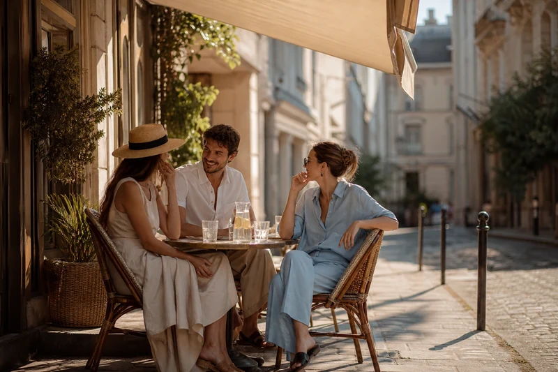 Trois personnes habillées en lin sur une terrasse parisienne ombragée en pleine canicule