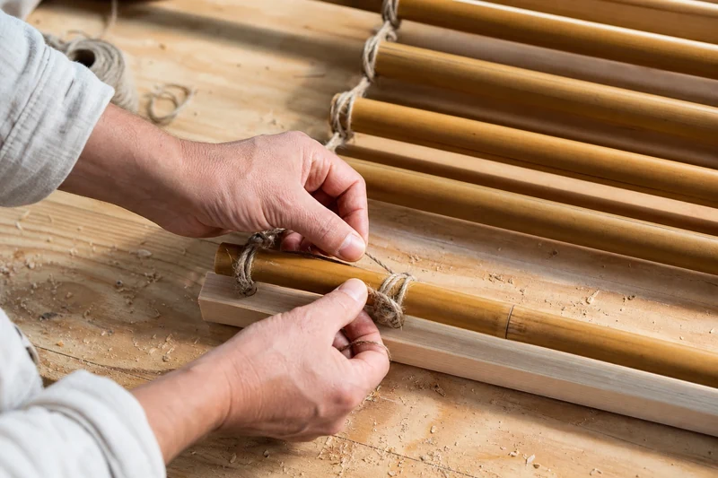 Étape de fabrication : nouage des cannes de bambou sur le tasseau supérieur du store