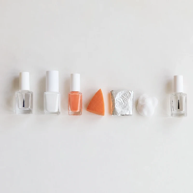 Matériel complet pour réaliser des aura nails à la maison : deux vernis, éponge triangulaire, base et top coat