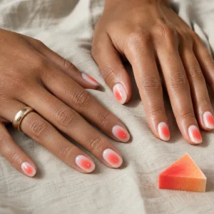 Mains bronzées portant des aura nails corail sur base milky avec halo lumineux au centre de chaque ongle
