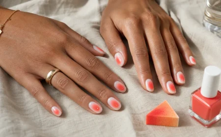 Mains bronzées portant des aura nails corail sur base milky avec halo lumineux au centre de chaque ongle