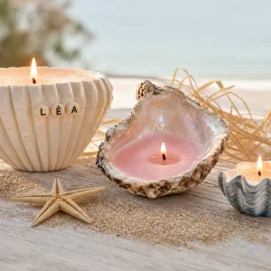 Trois bougies coquillages DIY allumées sur une table en bois avec perles-lettres formant un prénom