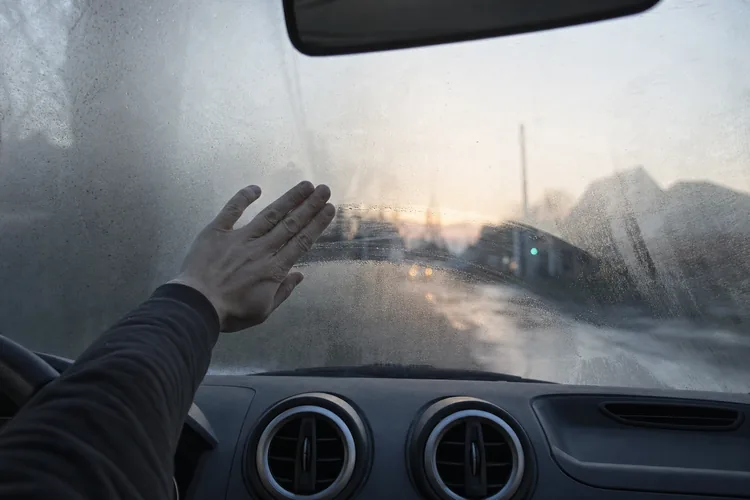 Main essuyant la buée sur un pare-brise embué de l'intérieur de la voiture