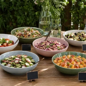 Buffet de salades d'été dressé sur table en bois dans un jardin, six saladiers colorés et étiquettes ardoise
