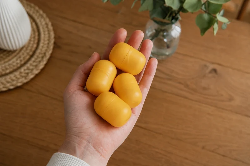 Quatre capsules jaunes vides de Kinder Surprise tenues dans une main au-dessus d'un plan de travail en bois