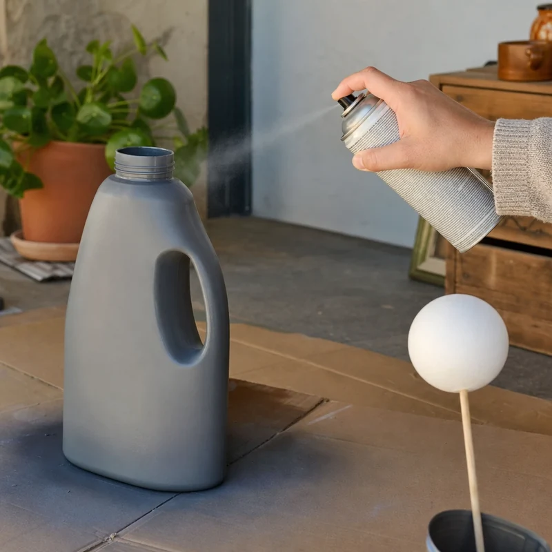 Application de peinture en bombe grise sur un bidon de lessive posé sur un carton
