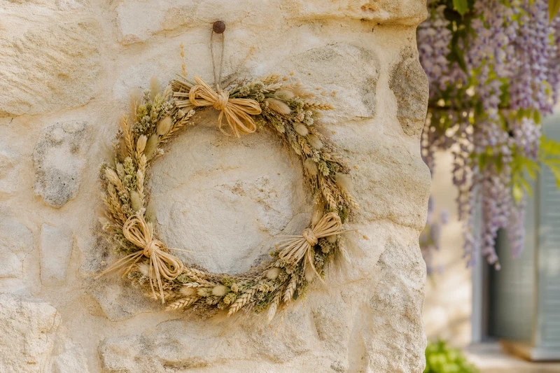 Couronne d'herbes fournie de 30 cm avec trois nœuds en raphia, sur mur en pierre provençale