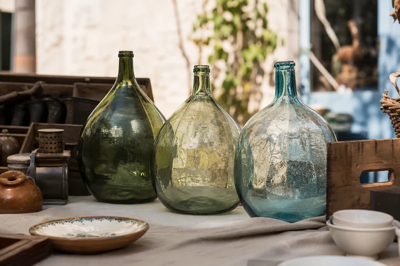Trois dames-jeannes en verre coloré sur un étal de brocante française en été