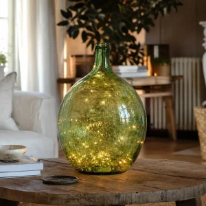Dame-jeanne en verre vert illuminée par une guirlande LED dans un salon français chaleureux