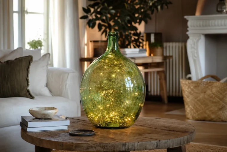Dame-jeanne en verre vert illuminée par une guirlande LED dans un salon français chaleureux