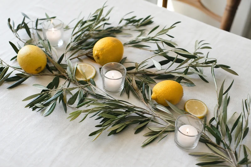Chemin de table naturel en branches d'olivier, citrons entiers et bougies sur nappe en lin