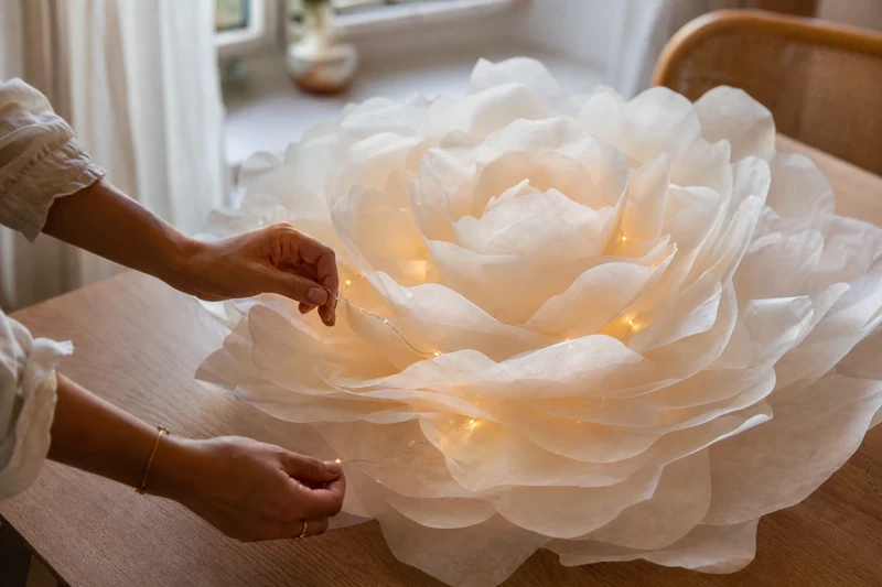 Glisser une guirlande LED dorée à piles entre les pétales de la fleur XXL en papier sulfurisé
