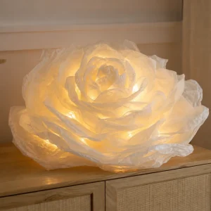 Grande fleur XXL en papier sulfurisé ivoire illuminée par une guirlande LED chaude, posée sur une commode en bois clair