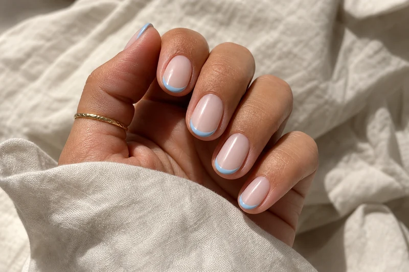 Micro-French bleu ciel pastel sur amande courte, base milky pink, main bronzée