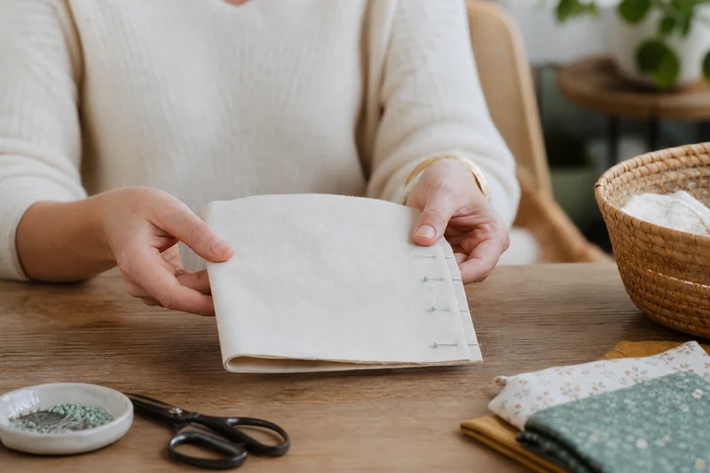 Mains pliant un rectangle de coton en deux, envers vers l'extérieur, épinglé sur le côté, étape 1 de la couture du sachet pyramide