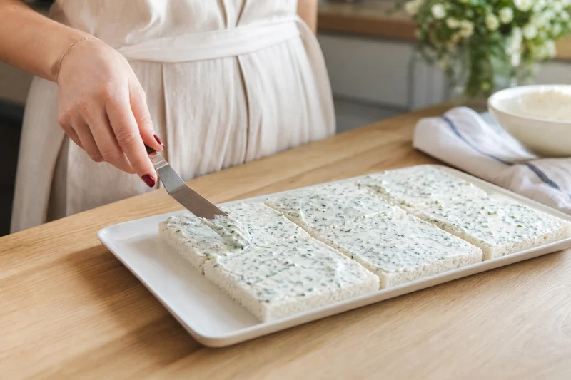 Étape de montage smörgåstårta : étaler la crème au fromage frais et aux herbes sur la première couche de pain de mie